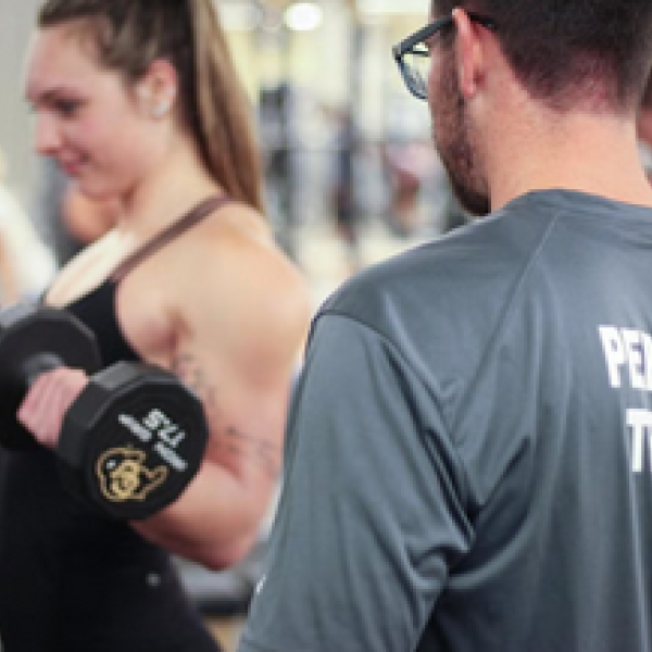 Personal trainer overseeing student lifting dumbells