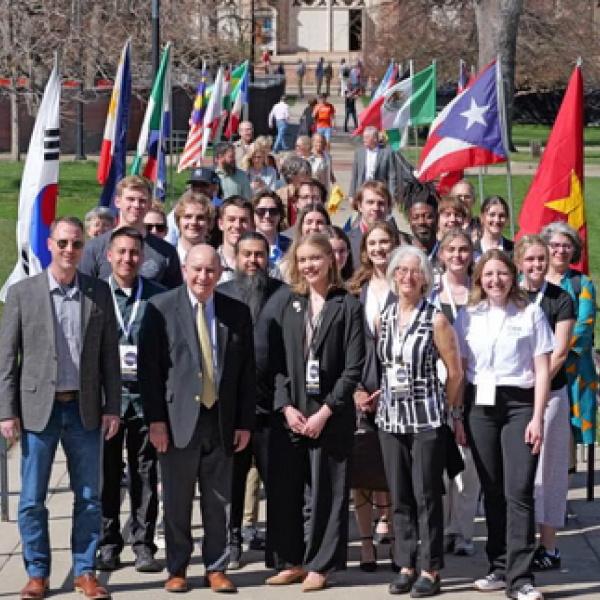 Group of CWA attendees standing on waking path on campus with different country flags lining the walkway