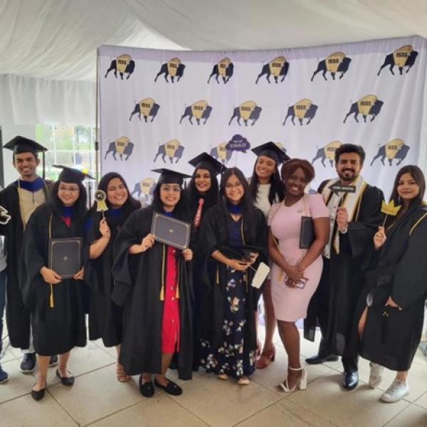 International students at reception posing for photo wearing cap and gown and holding signs in front of buffalo background