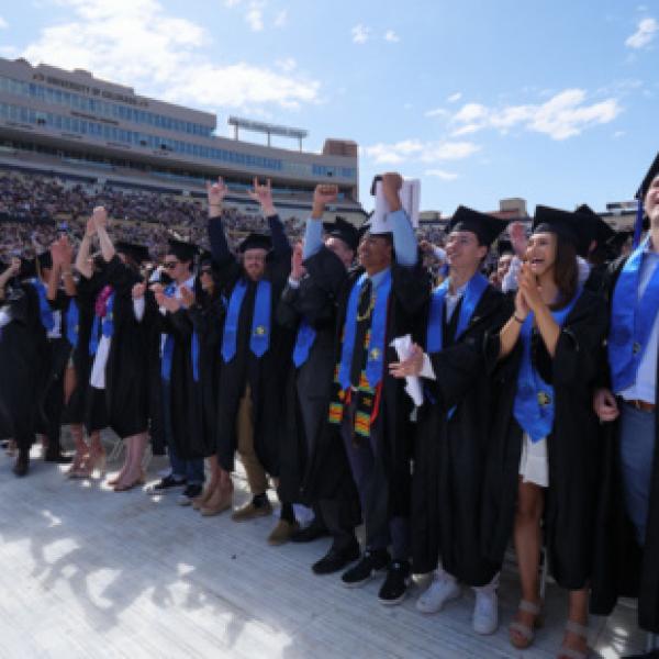 Students in cap and gown celebrating at Folsom Field