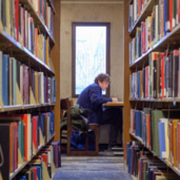 person sitting at table at the end of rows of library book shevlves