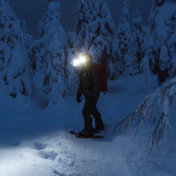 Person snow shoeing at night in a snowy forest with a head lamp on