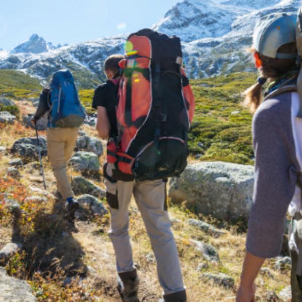 Three people hiking up a hill with mountains before them