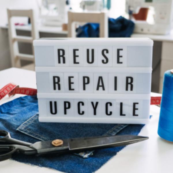 Reuse Repair Upcycle sign on a pair of cut jeans with scissors, thread, and a measuring tape