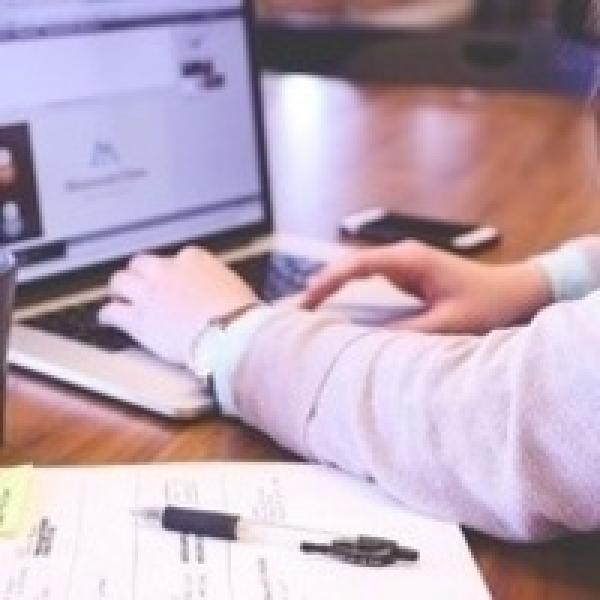Persons hand on laptop keyboard with notebook and pen next to laptop on table