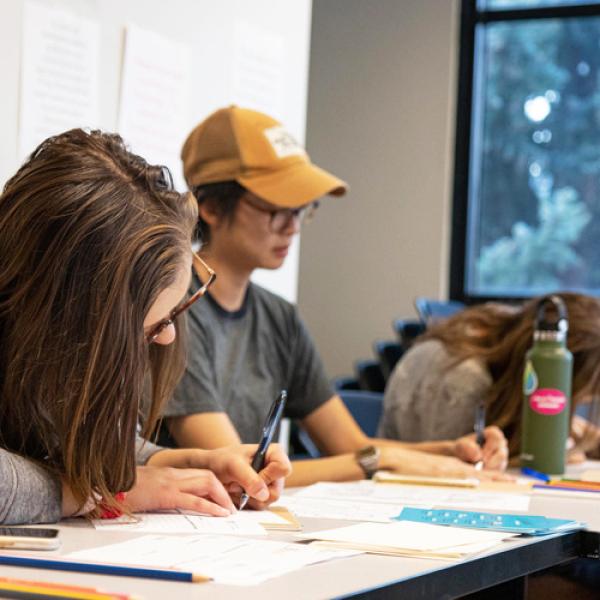 Students sitting at a table in a classroom writing