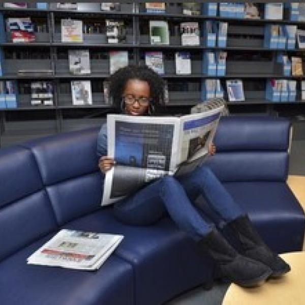 Person sitting on a couch in the Business Library reading a newspaper