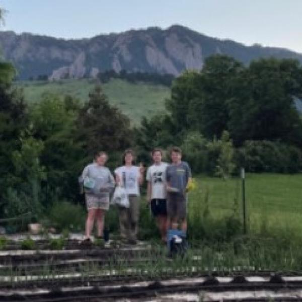 Four students standing in the Table Mesa Community Garden with the Flatirons in the background