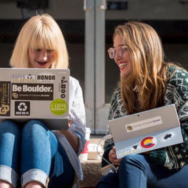 Two students working on laptops sitting outside