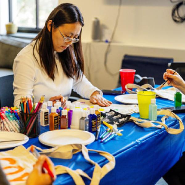 Three people sitting at craft table with art supplies and projects in front of them