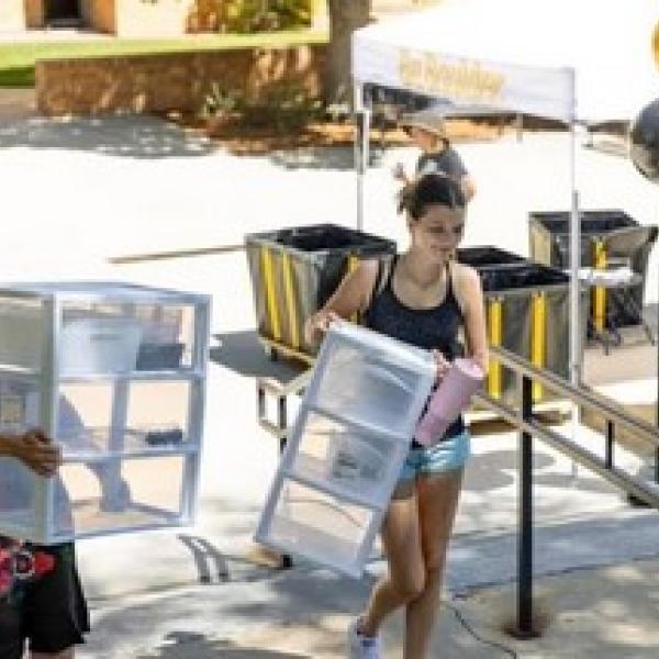 Two students carrying plastic storage drawers up stairs to residence hall