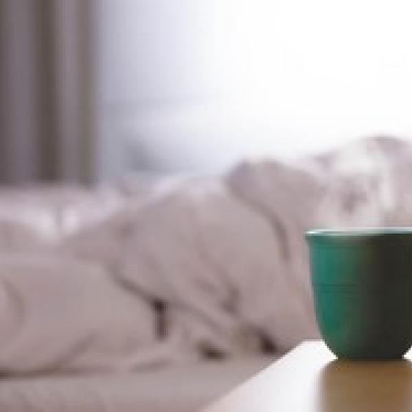 Mug on an end table with an unmade bed in the background