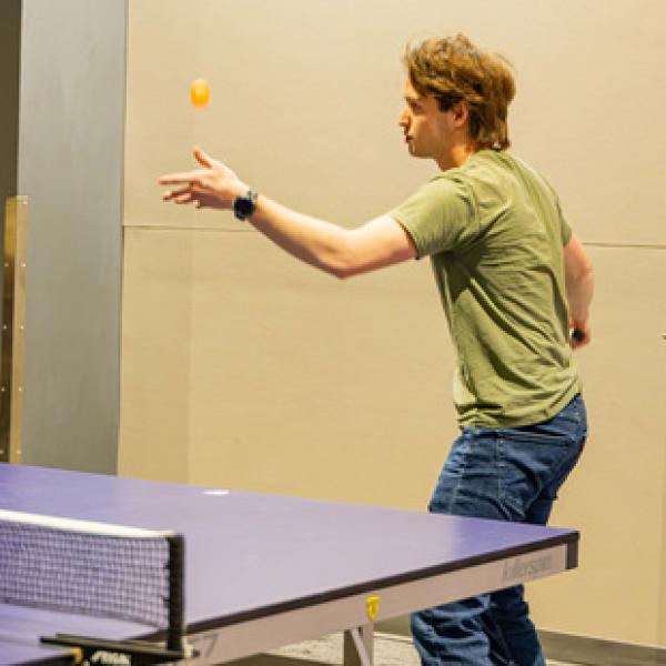 Person doing ping pong serve with ping pong table in front of him