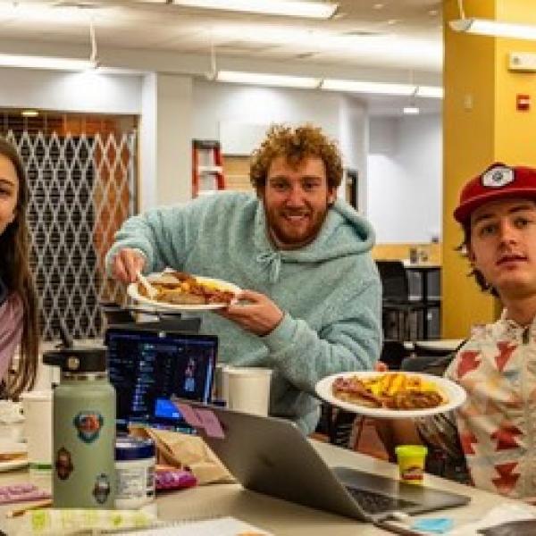 Students eating breakfast at a table with their laptops