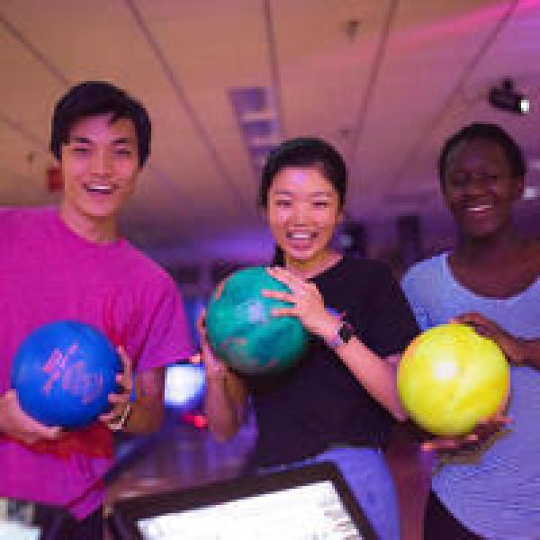 Photo of 3 people holding bowling balls at a bowling alley