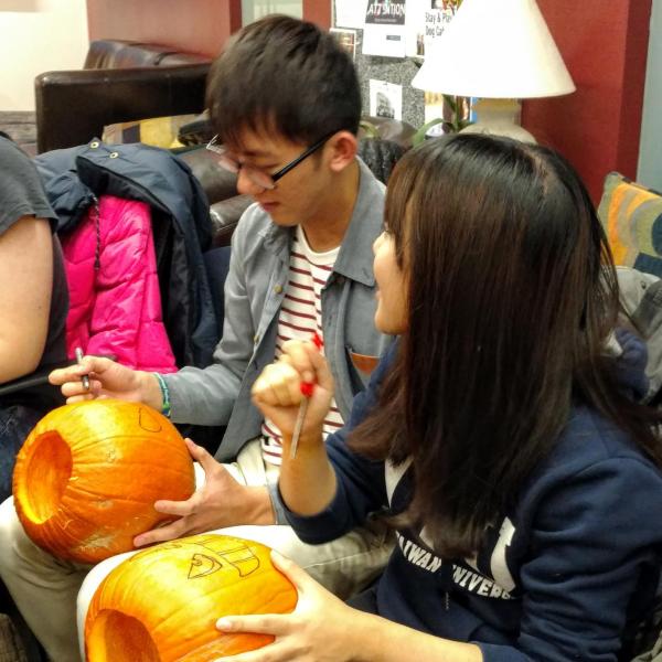 Two students drawing faces on pumpkins