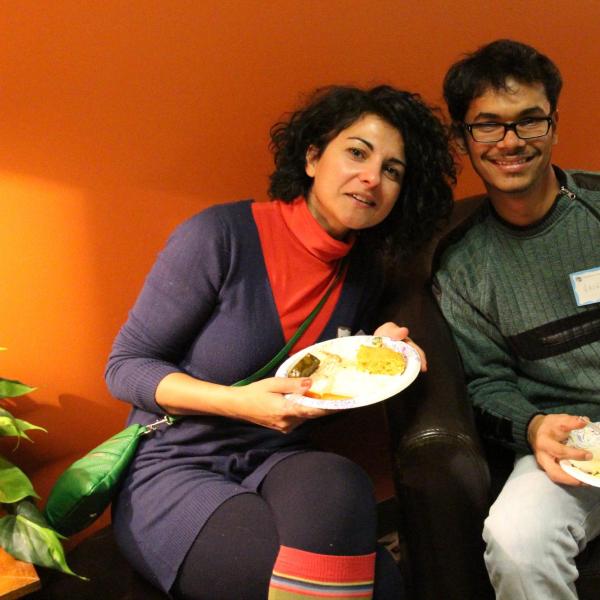 Two BFIS members in chair with food in front of red wall