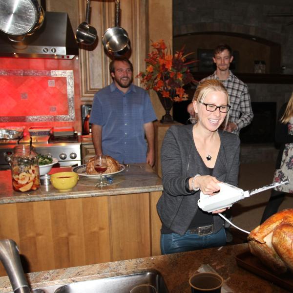 Person carving a turkey with others watching in the background