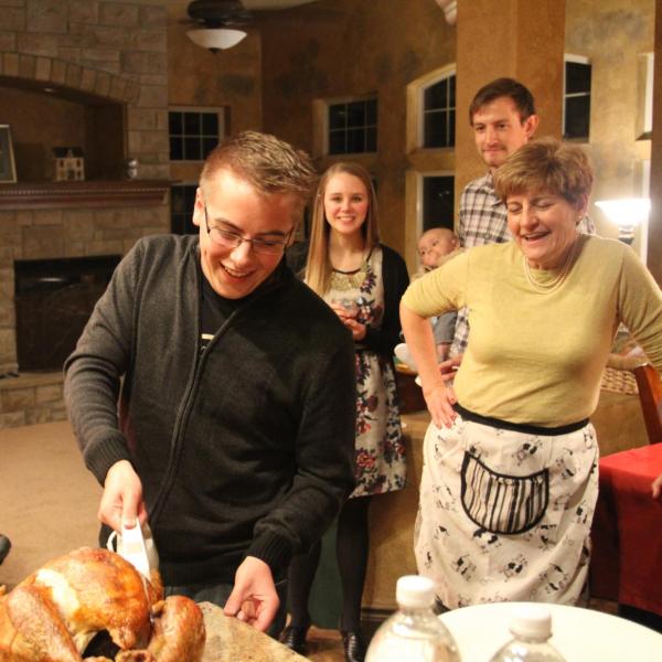 Student carving turkey with family watching in background