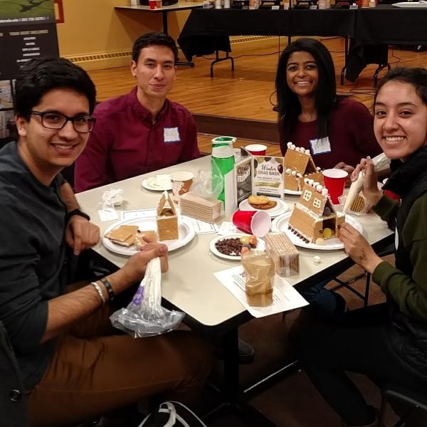 Four students smiling at table with their half finished gingerbread houses