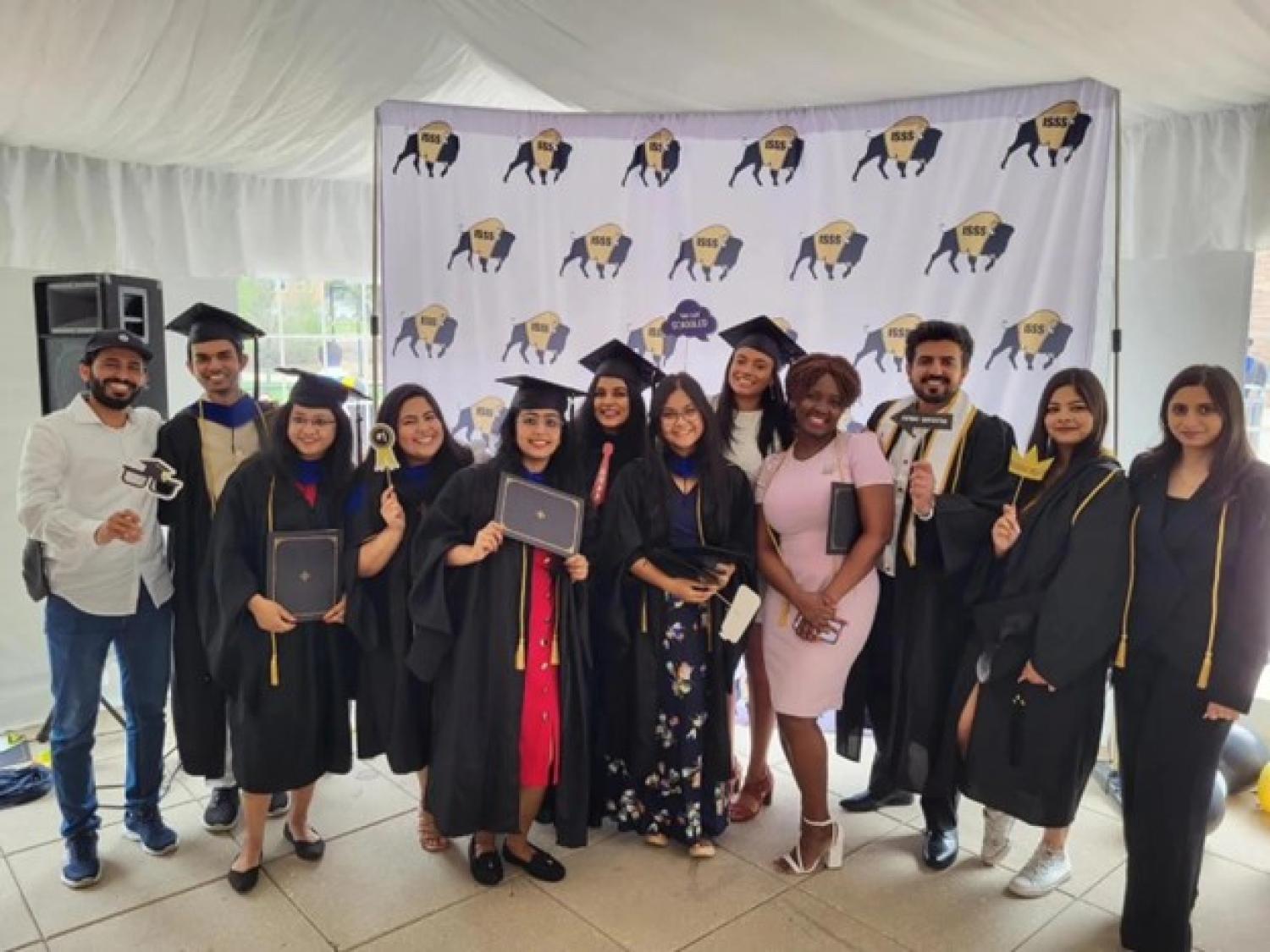 International students at reception posing for photo wearing cap and gown and holding signs in front of buffalo background