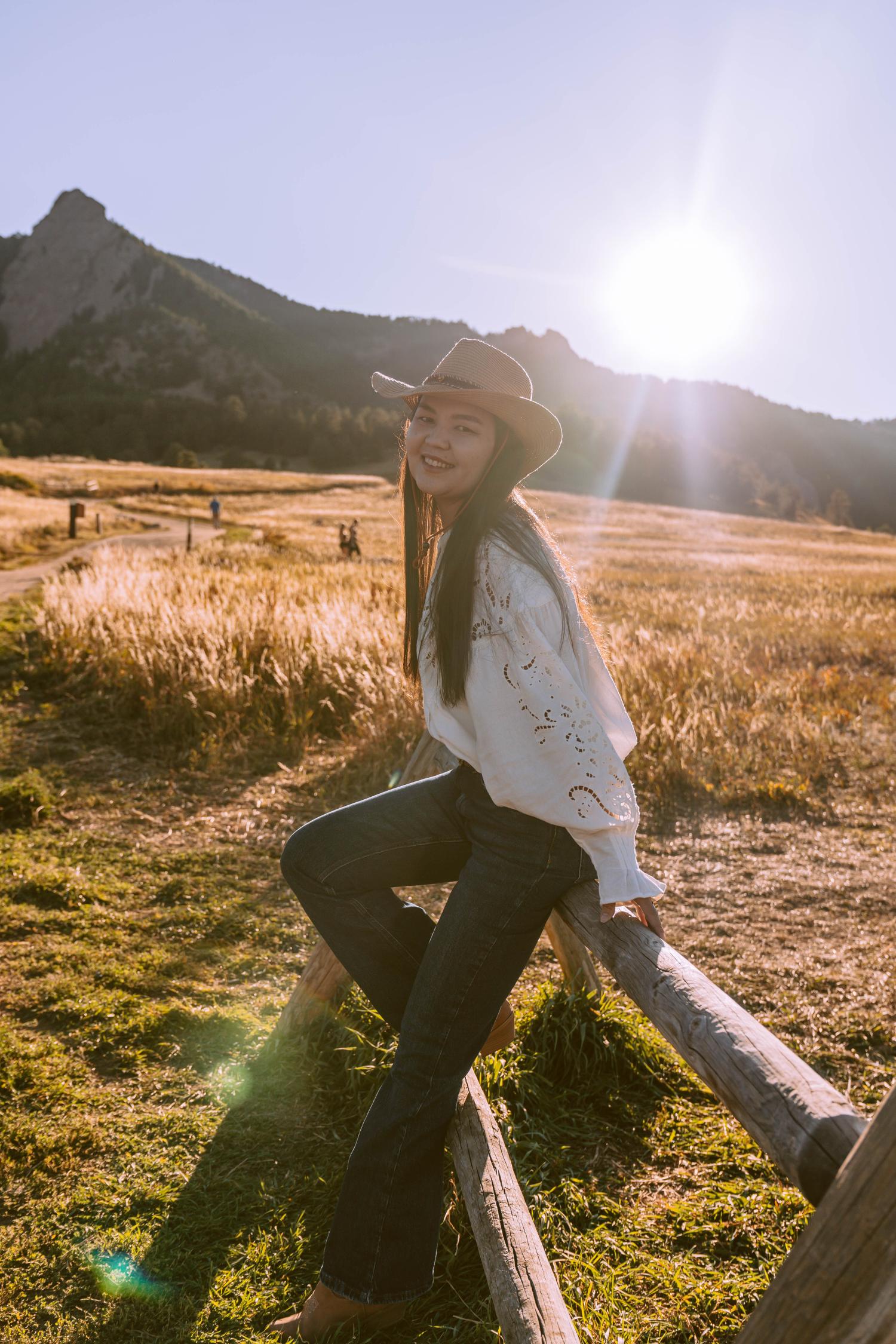 Zukhra Baibolatova posing on a wooden post fence wearing cowgirl hat at Chataqua Park with mountains in the backgroun