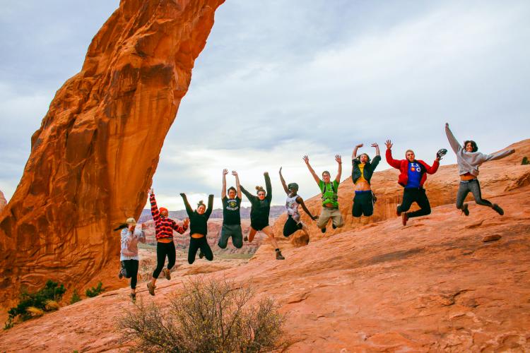 Students jumping with stone arch behind them