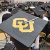 Graduation cap with gold CU letters and other graduates can be seen sitting in the background at the ceremony