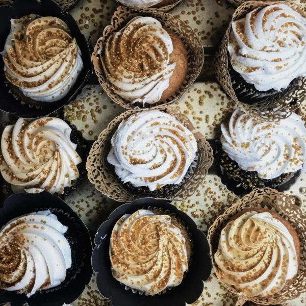 Cupcakes with white icing dusted with gold sprinkles. Cupcakes are lined in a row.