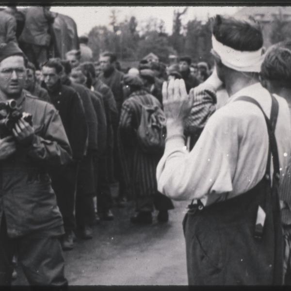 Philip Drell takes photographs of the surrender of Dachau camp guards while liberated prisoners look on.