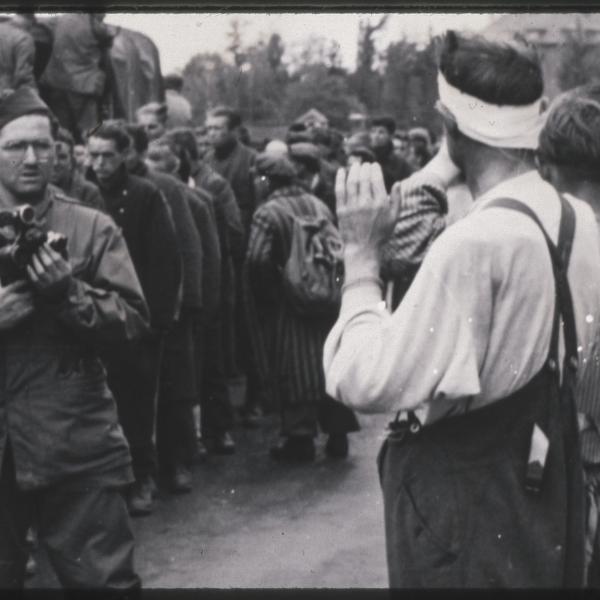 Philip Drell takes photographs of the surrender of Dachau camp guards while liberated prisoners look on.