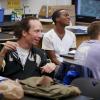 Students smiling and engaging in conversation with in a Jewish Studies class. 3 students sitting at desks, facing the teacher out of frame. They are smiling and laughing.