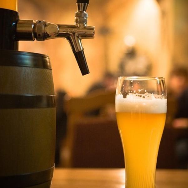 Wooden beer barrel with dispenser sitting on bar with tall glass of beer
