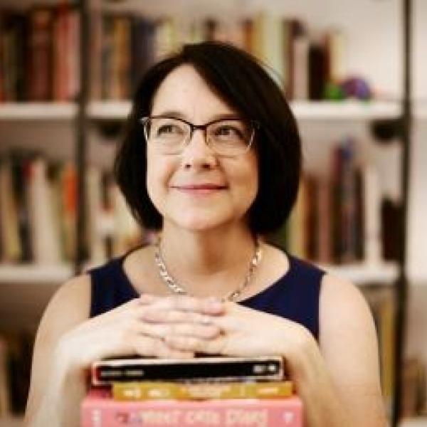 Professor Christine Larson smiling with her hands folded on top of a stack of books. (Credit: Jimena Peck)