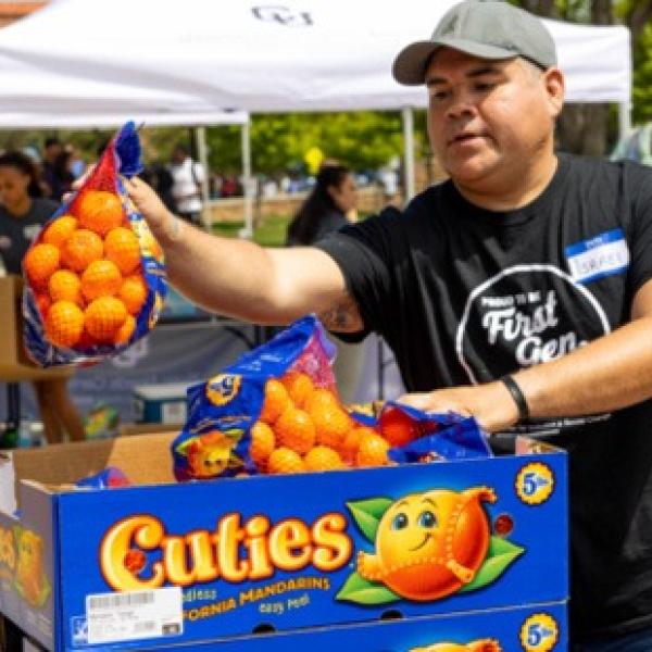 A man holding up a bag of mandarin oranges during an outdoor a food pantry event.