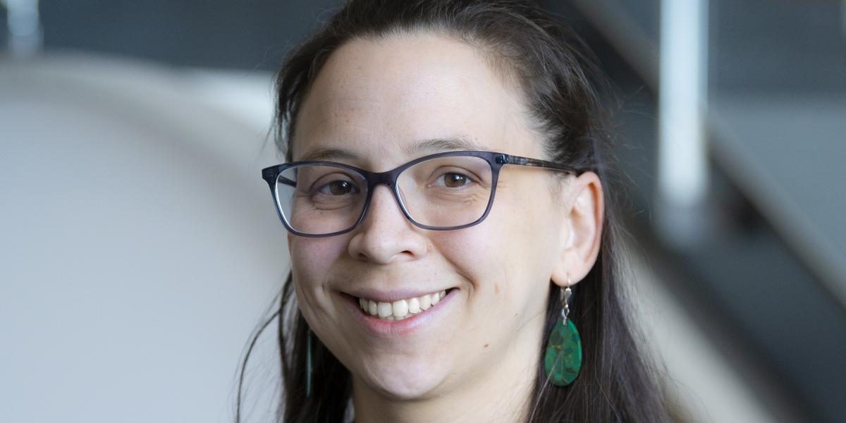 Picture of Konane smiling, she is wearing glasses and green earrings.