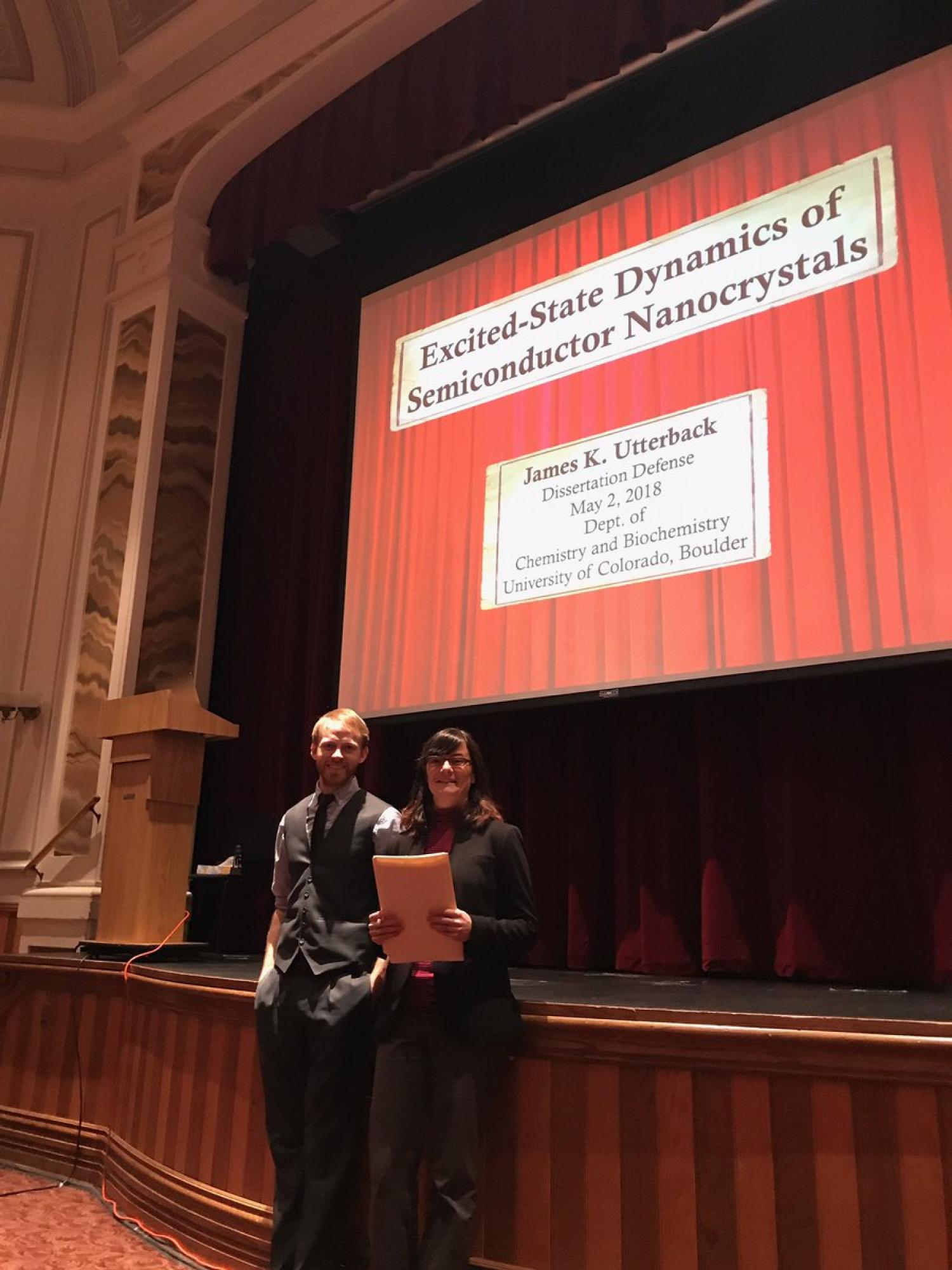 James and Gordana standing in front of the stage in the theater where James defended