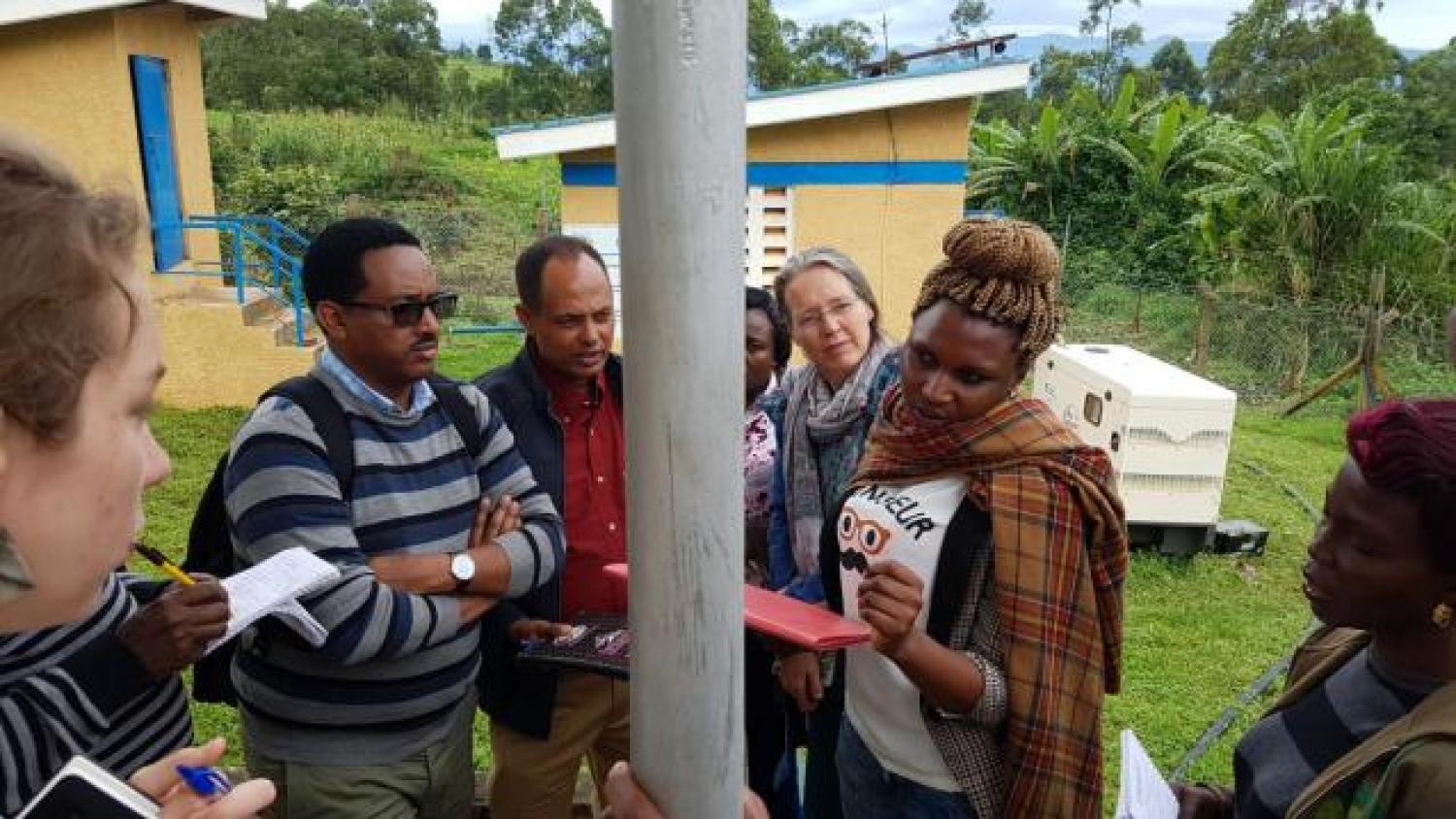 In Kabarole, Uganda, people stand around a solar-powered water pump and look at a sheet of paper.