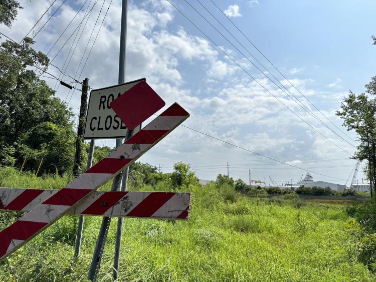 A road closed sign in a field, with industrial towers in the background