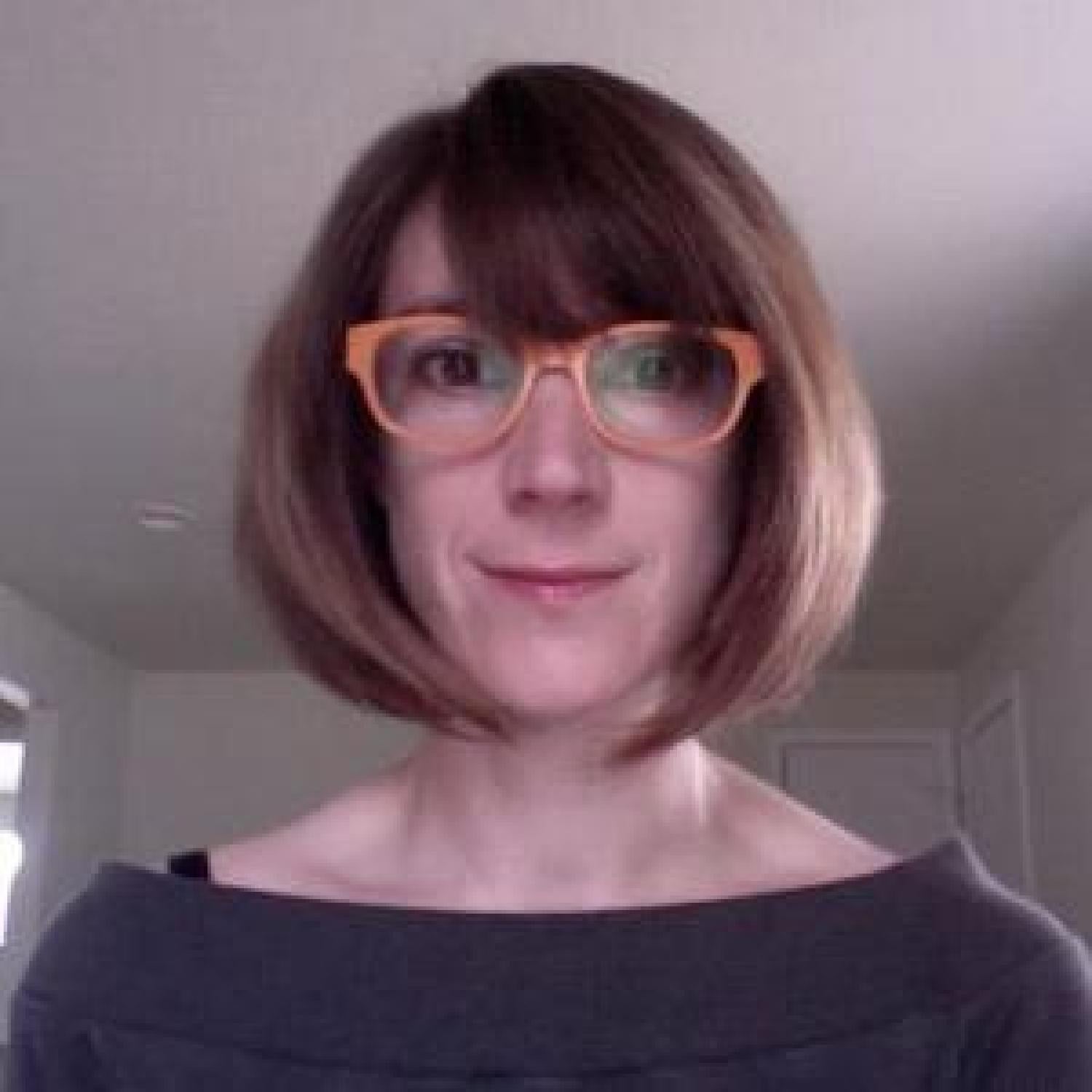 Dr. Lori Emerson looking at the camera in a shoulders-up shot. She is white, her hair is reddish brown and bobbed chin-length, and she is wearing orange glasses.