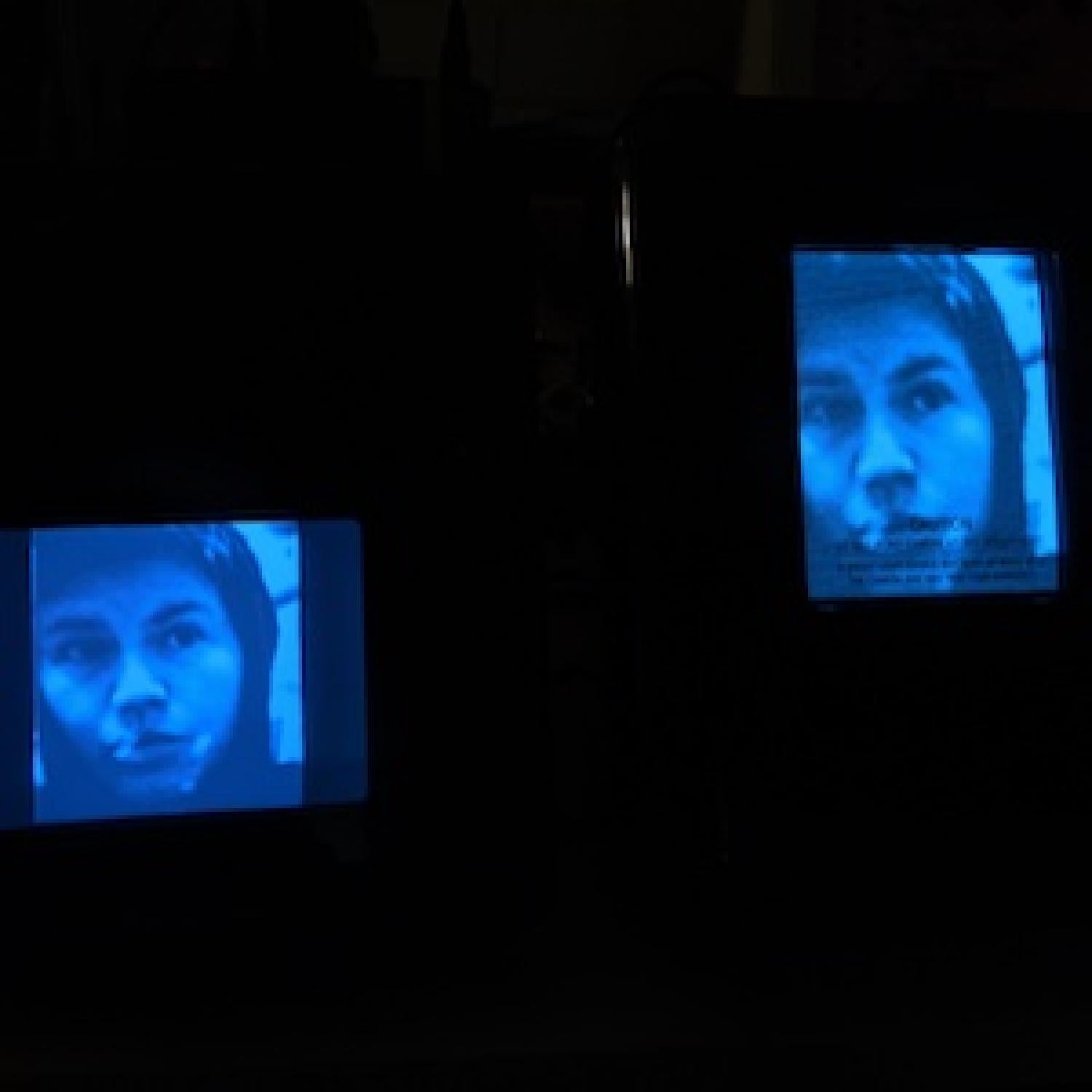 Dr. libi rose striegl appears in two blue-tinted low-res black and white images on small CRT screens. she is wearing a hoodie and looking to the side
