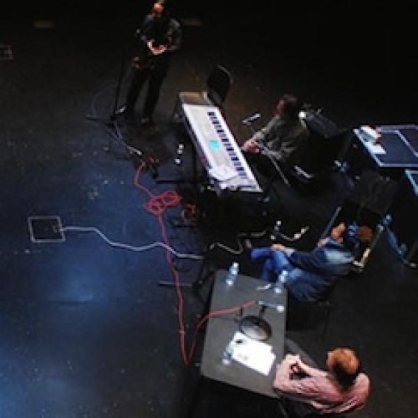 an areal view of a performance in black box theater. 4 digital performers, microphones and a keyboard.
