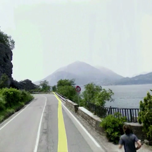 a road on the side of the mountain, body of water in center, mountain in background.
