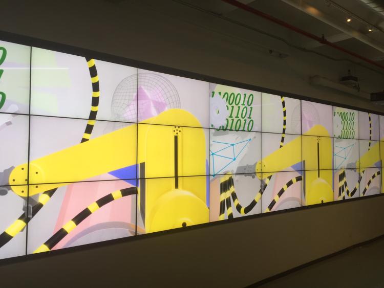 digital installation on many screen grid showing yellow machines, wires, wireframe heads and binary code