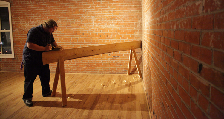 An artist marks a board in a gallery in preparation for an installation.