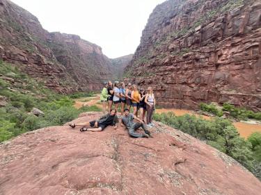 Students pose on a rock on the bank of the river.