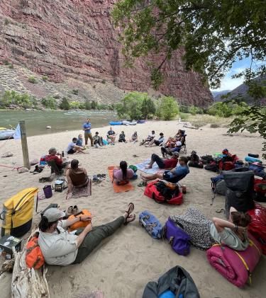 Students lounge on a river bank, watching a speaker