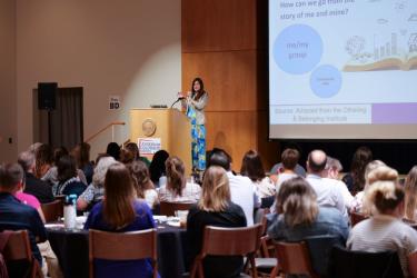 Juliana Tafur presenting the plenary at the Leadership Colorado Needs event on stage, speaking to a crowded room