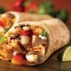 Stock photo of a burrito cut in half with limes on the cutting board next to the burrito halves