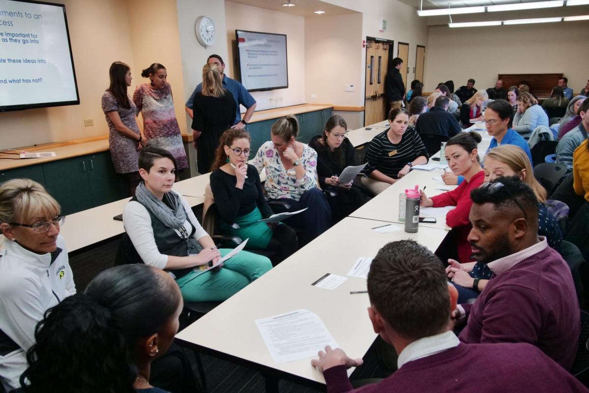 a group of employees are gathered around a table, having a discussion